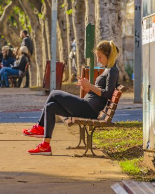 TEL AVIV, ISRAEL, Aralık 2019 - Parktaki bankta oturan sarışın genç bir kadın, Tel Aviv, İsrail 'de kokuşmuş bir yayaydı.