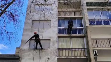 Düşük açılı çekim, güvenlik kabloları ile askıya alınan iki işçinin montevideo, uruguay 'daki bir apartman dairesinin ön cephesini temizlerken çekilmiş görüntüleri.