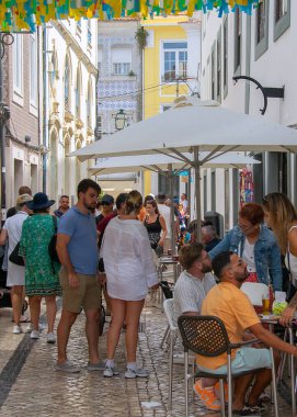 Aviero, Portekiz: 15 Ağustos 2023: Aveiro 'da eski bir kaldırım taşı caddesinde bir kafede oturan turistler, yukarıda renkli dekorasyonlarla neşeli bir hava yarattılar.