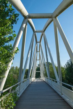 Isla de Soto 'da açık mavi gökyüzünün altında yemyeşil ağaçlarla çevrili beyaz metal bir yaya köprüsünün geniş açılı görüntüsü.