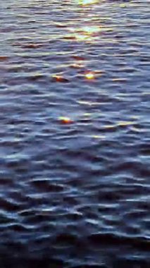 Günbatımında sakin bir denizin üzerinde güneş ışınlarının yansımasını gösteren sabit açılı bir kamerayla dikey bir video.