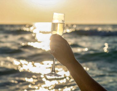 Orta açı, bir kadının kolunun denizin ortasından yukarı doğru yükseldiğini ve elinde şampanya bardağı tuttuğunu gösteriyor. 