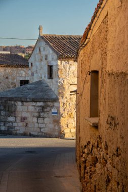 Sert taş evlerle kaplı dar asfalt bir caddenin dikey görüntüsü. Sahne, geleneksel bir İspanyol köyünün ya da eski bir kasabanın kırsal cazibesini ve sakin atmosferini yakalıyor..