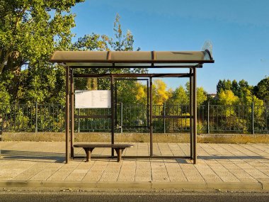 Zamora 'daki metal ve cam otobüs durağı barınağının geniş bir önü. Boş yapı, güneşli bir günde yeşil ağaçların ve çitlerin önündeki bir çakıl tarlasında duruyor..