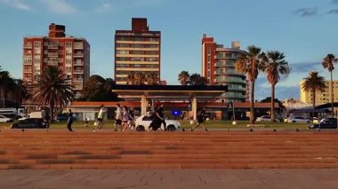 Montevideo, Uruguay: 18 Ocak 2026: Montevideo Rambla 'sında bir yaz öğleden sonrasını gösteren hafif bir zoom ile sabitlenmiş kamera videosu. İnsanlar arka planda binalar ve cadde boyunca yürüyorlar.
