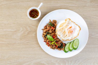 Üzerine kızarmış fesleğen ve ahşap bir masada kızarmış yumurta konmuş pirinç.