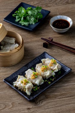 Buharda pişirilmiş hamur köfteleri siyah bir seramik tabakta servis ediliyor. Sos ve yemek çubukları, Asya yemekleri ahşap masadaki yaşam fotoğrafçılığı, minimal ve zarif bir stil.