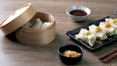 Buharda pişirilmiş hamur köfteleri siyah bir seramik tabakta servis ediliyor. Sos ve yemek çubukları, Asya yemekleri ahşap masadaki yaşam fotoğrafçılığı, minimal ve zarif bir stil.