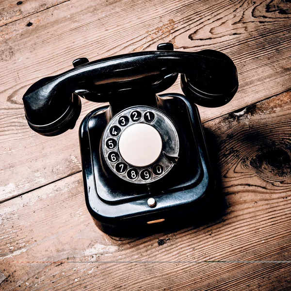 Old black phone with dust and scratches on wooden floor — Stock Photo, Image