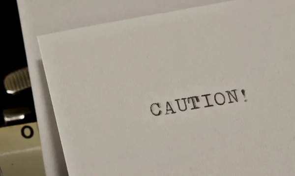 Caution text typed on old black typwriter — Stock Photo, Image