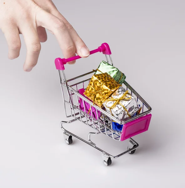 Pink shopping cart in woman hand and blue gift — Stock Photo, Image