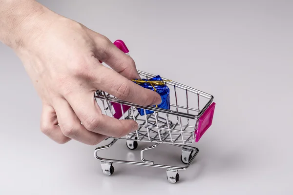 Růžový nákupního košíku v ženě ruku a modré dárek — Stock fotografie