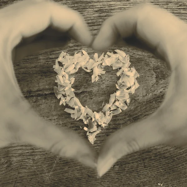 Un corazón de pétalos acostado en una mesa de madera y manos — Foto de Stock