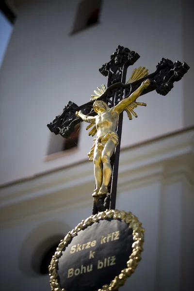 Cruz preta com jesus de ouro e capela como fundo — Fotografia de Stock