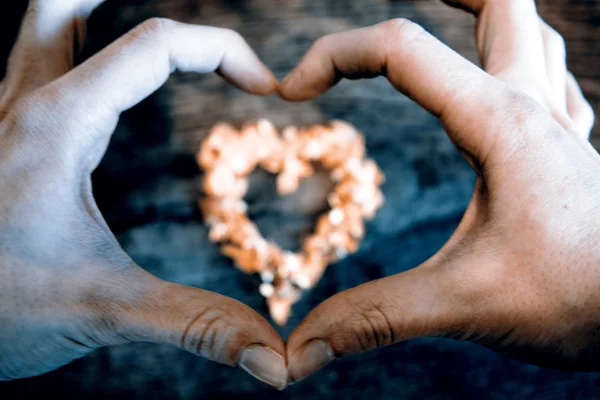 Um coração de pétalas que jazem em uma mesa de madeira e mãos — Fotografia de Stock