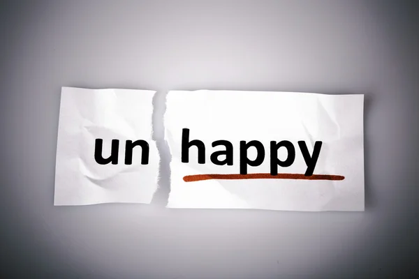 The word unhappy changed to happy on torn paper — Stock Photo, Image