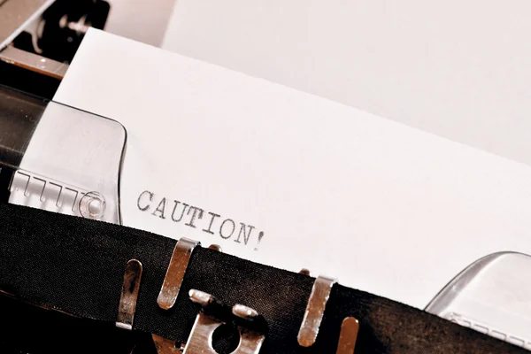 Texto de cautela digitado na velha máquina de escrever preta — Fotografia de Stock