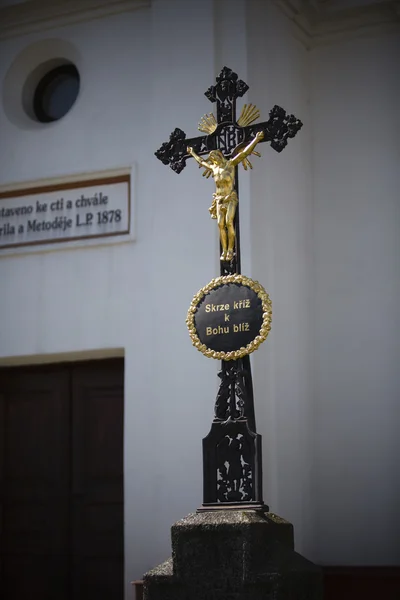 Cruz preta com jesus de ouro e capela como fundo — Fotografia de Stock