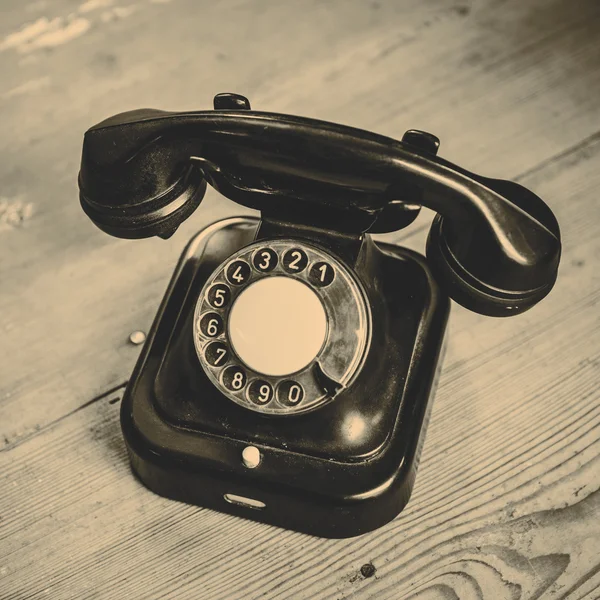 Oude zwarte telefoon met stof en krassen op houten vloer — Stockfoto