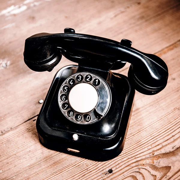Old black phone with dust and scratches on wooden floor — Stock Photo, Image