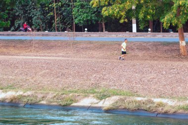 KANCHANABURI / THAILAND-MAY 7. 2020: Tayland 'ın Kanchanaburi kentinde 7 Mayıs 2020 tarihinde Mae Klong Barajı' ndaki sulama kanalının yanında sağlıklı bir yolda koşan tanımlanamayan Taylandlı sporcular.