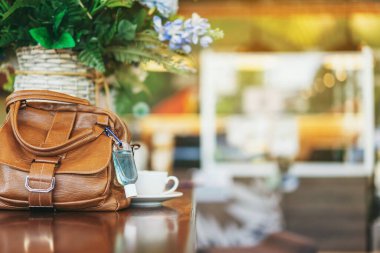 Corona Virüsü 'nü (Covid-19) öldürmek için mini alkol jeli şişesi kafede üzerinde sıcak kahve olan kahverengi deri bir omuz çantasına asılır. Yeni normal yaşam tarzı. Sağlık hizmetleri kavramı. Alkol jeline odaklanın.