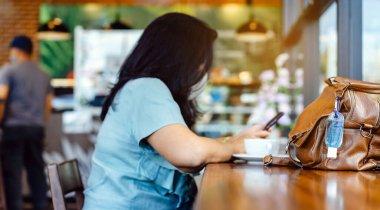 Corona Virüsü 'nü (Covid-19) öldürmek için mini alkol jeli şişesi kafede üzerinde sıcak kahve olan kahverengi deri bir omuz çantasına asılır. Yeni normal yaşam tarzı. Sağlık hizmetleri kavramı. Alkol jeline odaklanın.