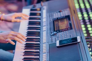 Müzisyen, konser sahnesinde çalmak için akıllı telefonu kılavuz olarak kullanarak elektronik klavye sentezleyicileri çalar. Akıllı telefona seçici odaklanma.