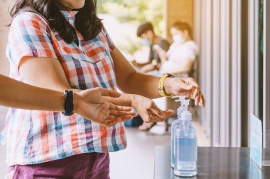 Kadının elleri kahve dükkanına girmeden önce Coronavirus 'un (Covid-19) yayılmasını önlemek için mavi alkol jeli şişesine bastı. Yeni normal yaşam tarzı. Alkol jeli şişesine odaklan.