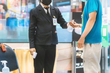 Müşterinin eli, alışveriş merkezine girmeden önce mikrop ve bakteri bulaşmasını önlemek ve Corona virüsünü (Covid-19) önlemek için kadın güvenlik görevlisinden bir damla alkol almayı bekliyor..