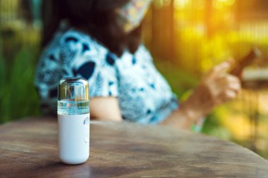 Corona virüsünün (Covid-19) arka planda cep telefonu kullanan bir kadının bulanık görüntüsüyle masaya konmasını önlemek için el temizleme için alkol nano spreyi. Modern sağlık teknolojisi.