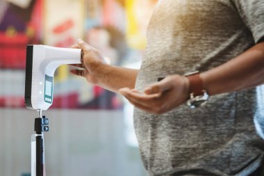 Koruyucu maskeli müşteri, bölgeye girmeden önce ısı tarama makinesiyle dijital termometreye el kaldırdı. Enfeksiyon kapmış kişilerin yasak bölgelere girmesini önlemek için tarama.