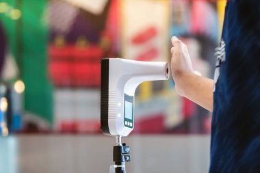 Koruyucu maskeli müşteri, bölgeye girmeden önce ısı tarama makinesiyle dijital termometreye el kaldırdı. Enfeksiyon kapmış kişilerin yasak bölgelere girmesini önlemek için tarama.