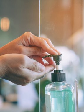 Coronavirus 'un (Covid-19) kafeteryaya girmeden önce yayılmasını önlemek için yaşlı kadının elleri mavi alkol jeli şişesine basıldı. Sağlık sigortası konsepti. Yeni normal yaşam tarzı. Seçici odak