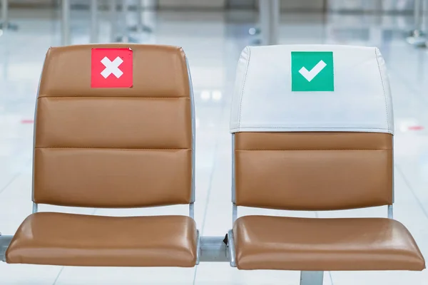 Rows empty brown chairs with the sticker sign sitting position for social distancing in waiting terminal of the airport to prevent of Corona virus (Covid-19). Safe travel new normal social distancing.