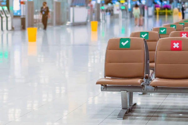 Rows empty brown chairs with the sticker sign sitting position for social distancing in waiting terminal of the airport to prevent of Corona virus (Covid-19). Safe travel new normal social distancing.