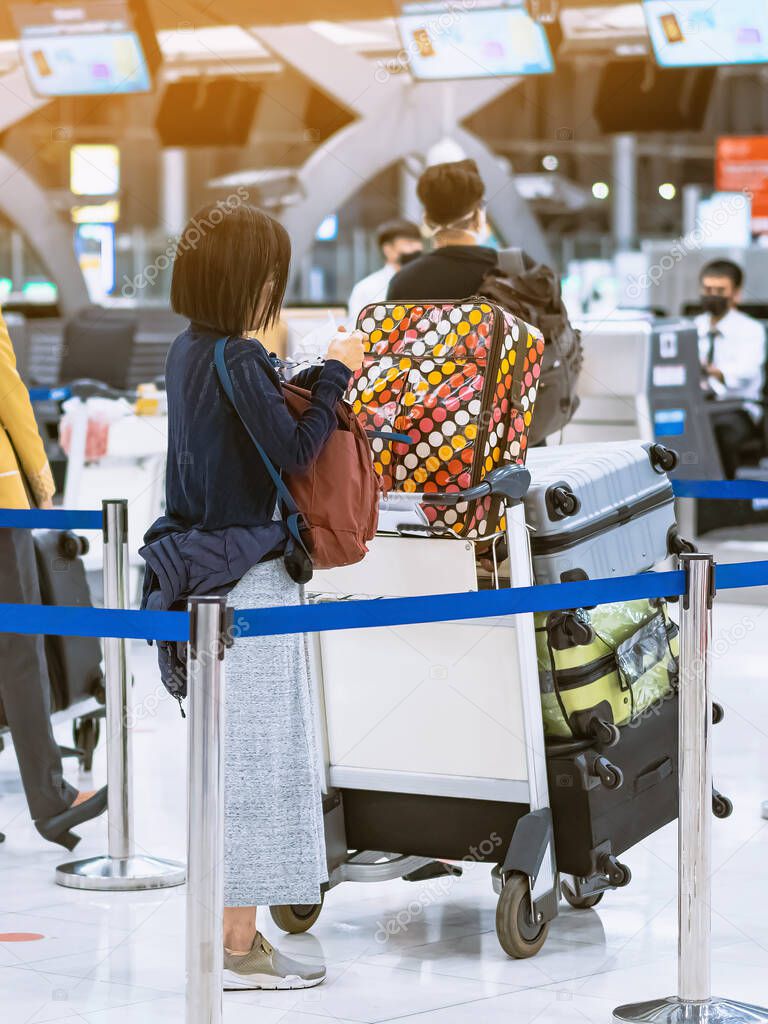 Back view of airline passenger wear face mask to prevent Corona virus (Covid-19) wait to check in counter in airport with staff wear face mask. New normal concept of travel after Covid-19 pandemic.