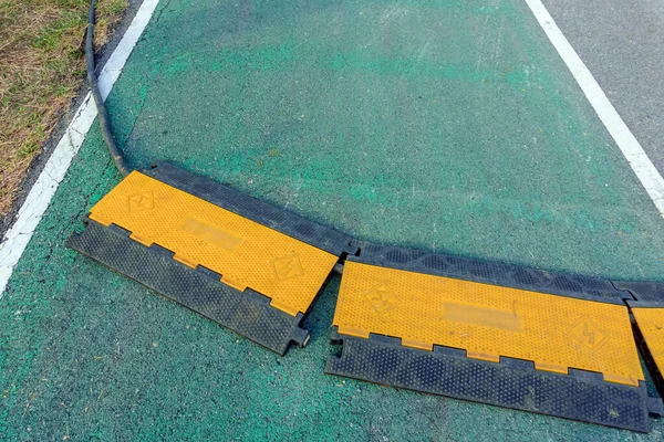Black and yellow heavy plastic covers for people and vehicle to cross over cables laid on road. Pavement pads to protect electrical wiring on sidewalk in public park. Channel for laying the wires.