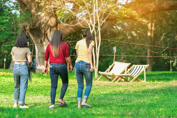 Back view of Asian woman with friends walking together on lawn through green garden.Female relaxing in park. Happiness friends spending time together outside in green nature. Enjoying nature outdoors.