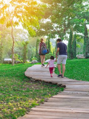Asyalı Baba 'nın yeşil bahçede yürüyen güzel kızını tutuşu. Baba ve kızı parkta birlikte yürüyorlar. Mutlu aile, yeşil doğada birlikte vakit geçiriyor..