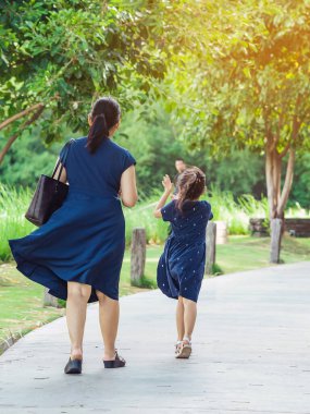 Annemizin mavi elbiseli güzel kızı yeşil bahçede yürürken görüntüsü. Anne ve kızı parkta birlikte yürüyorlar. Mutlu aile dışarıda yeşil doğada birlikte vakit geçiriyor..