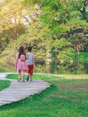 Asyalı genç kız ve oğlanın yeşil bahçede birlikte yürüdükleri arka plan görüntüsü. Kız ve erkek kardeş parkta birlikte yürüyorlar. Mutlu aile, yeşil doğada birlikte vakit geçiriyor..