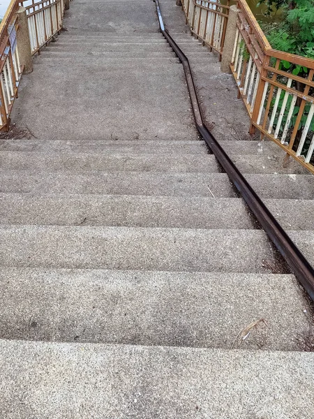 Stair-safe bike ramp along stairs. Comfortable and safe lanes for bicycles on stairs. Old and rusted steel rails for bicycles up and down for comfort between steps on stairs in the public park.