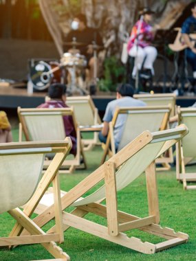 Bahçede akşam yemeği için masaları olan birçok beyaz iskemle arka planda müzikal performansın bulanık görüntüsüne sahip gölgeli yeşil çimlerle çevrilidir. Bahçedeki bahçe teras sandalyelerinde rahattır..