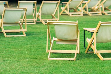 Çimenli masaları olan birçok boş beyaz iskemle gölgeli yeşil çimlerle çevrilidir. Bahçedeki teras sandalyelerinde rahat. Parktaki çim sandalyeleri. Bahçedeki güneş yatakları. Seçici odak.