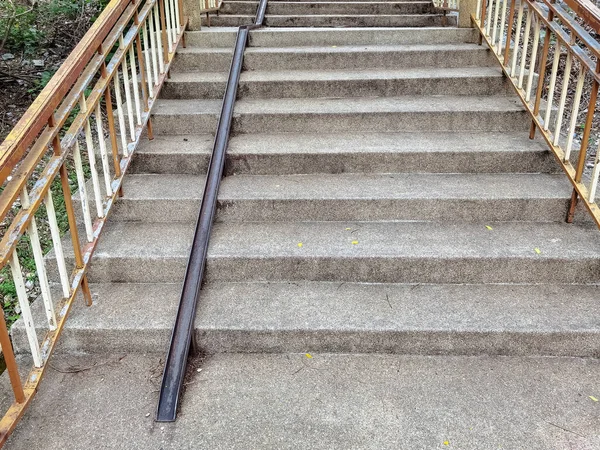 Stair-safe bike ramp along stairs. Comfortable and safe lanes for bicycles on stairs. Old and rusted steel rails for bicycles up and down for comfort between steps on stairs in the public park.