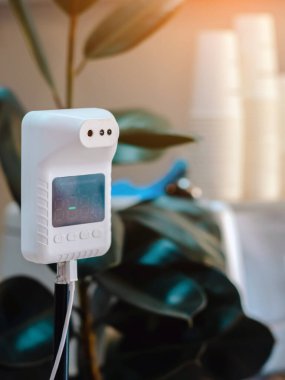 Vücut sıcaklığını ölçmek için Covid-19 salgını sırasında müşterilerin zorunlu kontrolleri için bir kahve dükkanındaki alıcının üzerine bir el koyarak vücut sıcaklığını ölçen dijital otomatik vücut ısısı makinesi..