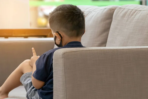 Widok Tyłu Azjatyckiego Chłopca Nosić Maskę Twarzy Odgrywa Smartfona Kanapie — Zdjęcie stockowe