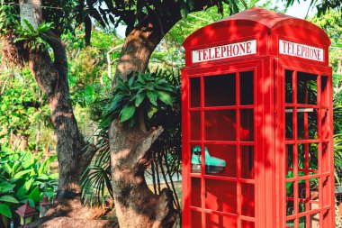 Bahçede kırmızı, Londra tarzı telefon kulübesi. Parktaki geleneksel İngiliz klasik telefon kulübesi yemyeşil ve ağaçlarla çevrili. Eski moda İngiliz telefon kulübesi. Klasik kırmızı telefon kulübesi.