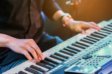 Erkek müzisyenin elleri konser sahnesinde dijital elektronik klavye sentezleyicilerine basıyor. Piyanist elleri elektronik piyanonun anahtarlarını çalar. Piyano çalan piyanist. Eldeki seçici odaklanma.